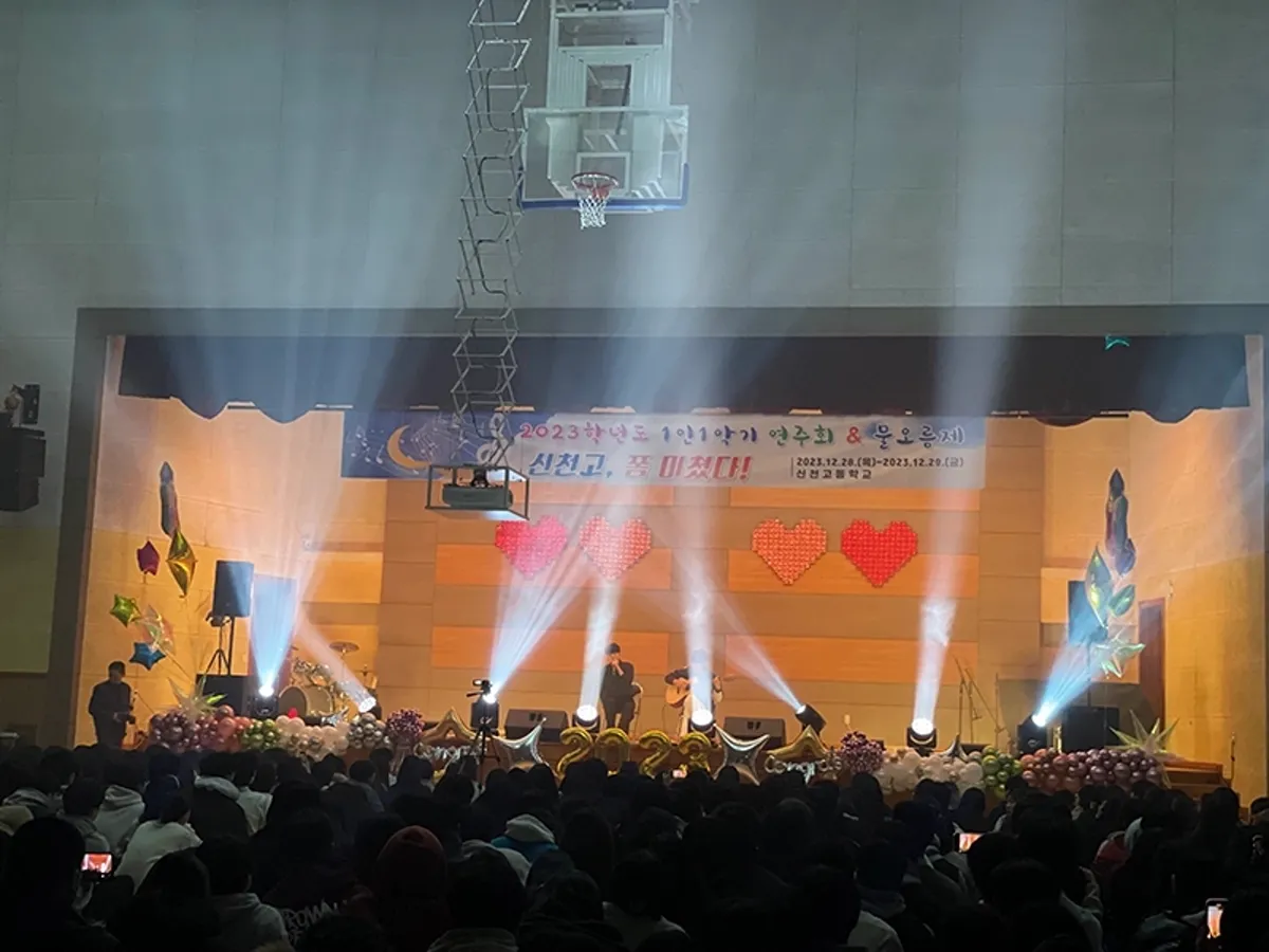 큰 공연장 무대에 조명 빔이 뻗고 객석이 가득 찬 모습을 뒤에서 찍은 장면
