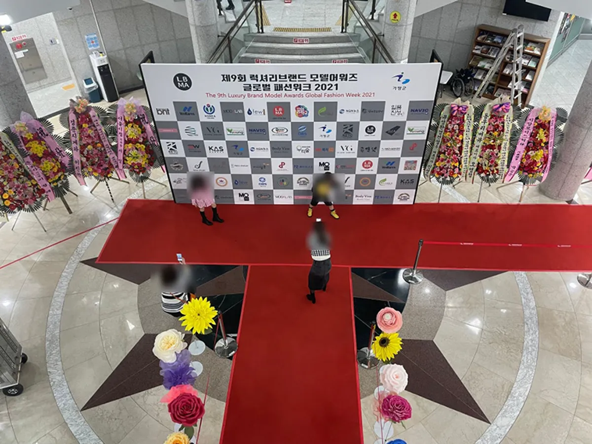 실내 로비 가운데 레드카펫 T자 길과 포토월, 화환이 놓인 행사 세팅을 위에서 본 모습